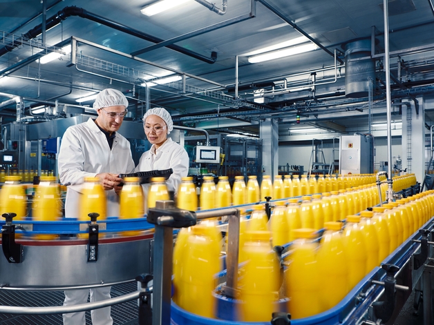 Due tecnici in un impianto di produzione di bevande che controllano il processo di riempimento di succo d'arancia.