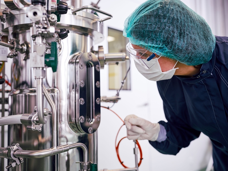 Scienziato con un fermentatore per la produzione biofarmaceutica Fermentatore e scienziato in un ambiente di produzione biofarmaceutica