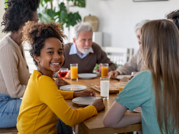 Giovane ragazza che sorride alla fotocamera mentre è seduta al tavolo da pranzo con la sua famiglia.