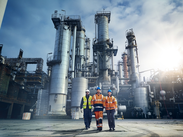 Three engineers walk across a refinery.